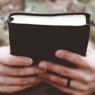 Someone holding a Bible wearing fatigues